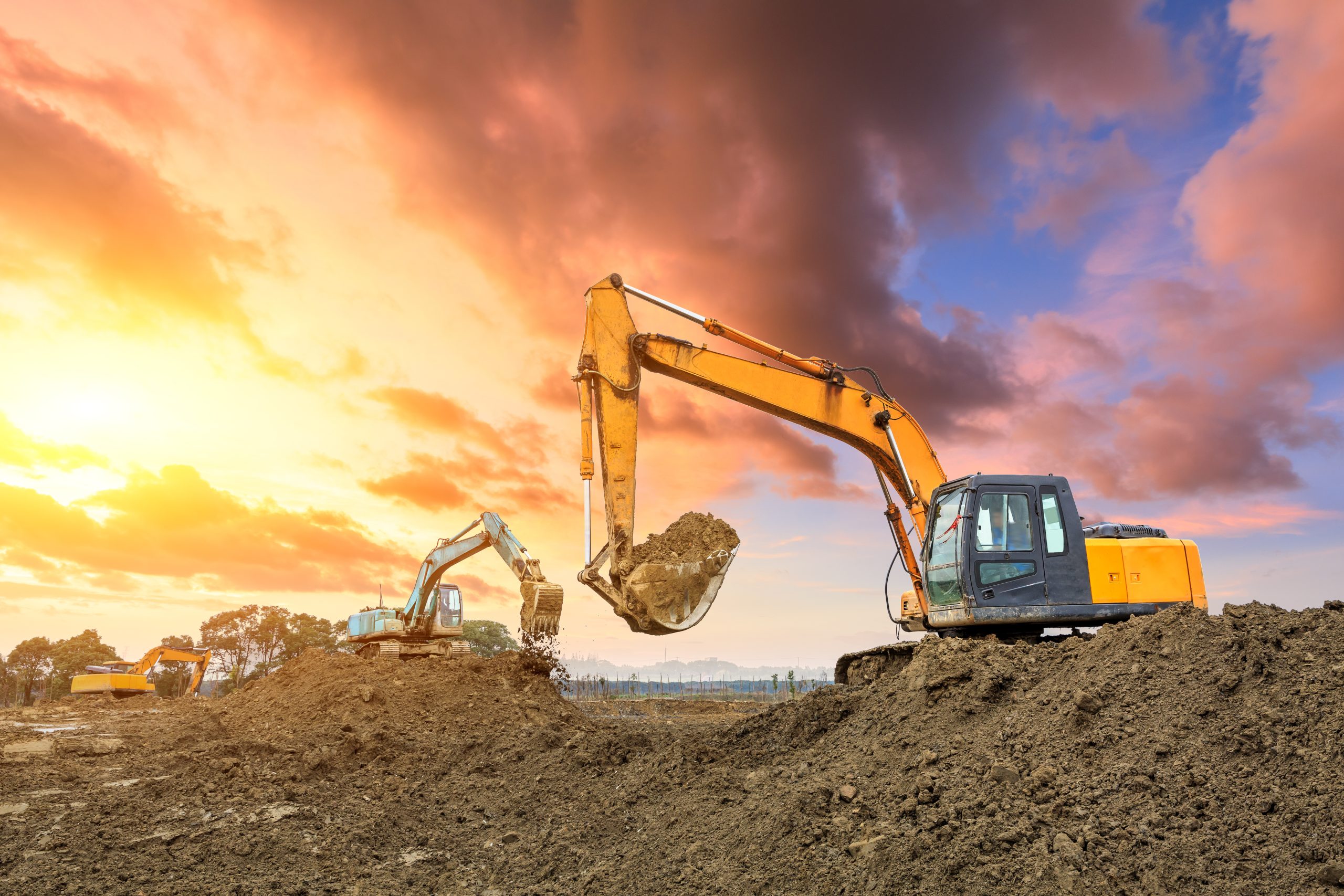 Three excavators work on construction site at sunset